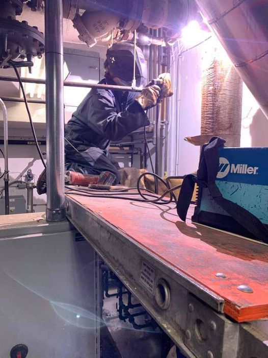 Un homme soude un tuyau sur un échafaudage dans une usine.