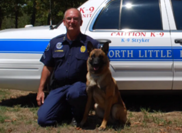 Police officer kneels beside a K-9 dog in front of a North Little Rock patrol car.