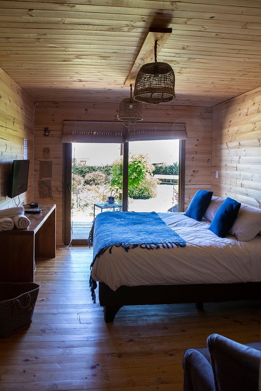 Dormitorio con paredes de madera, cama y puertas de cristal abiertas. Manta y almohadas azules.
