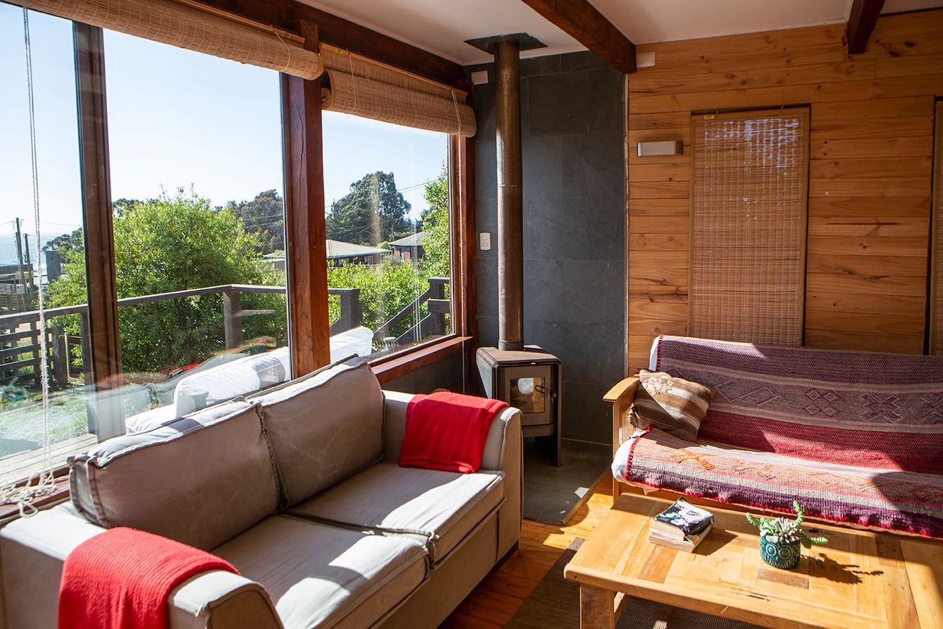 Acogedora sala de estar con sofás, ventana con vista a los árboles, paneles de madera y una pequeña estufa.