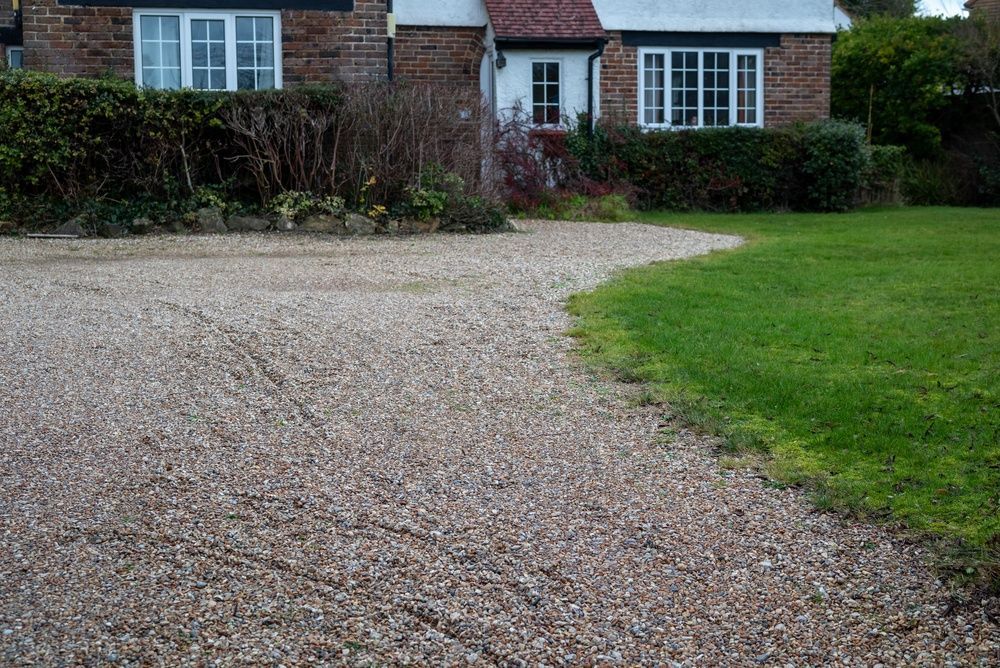 Gravel driveway curving toward a brick house with a green lawn and hedges