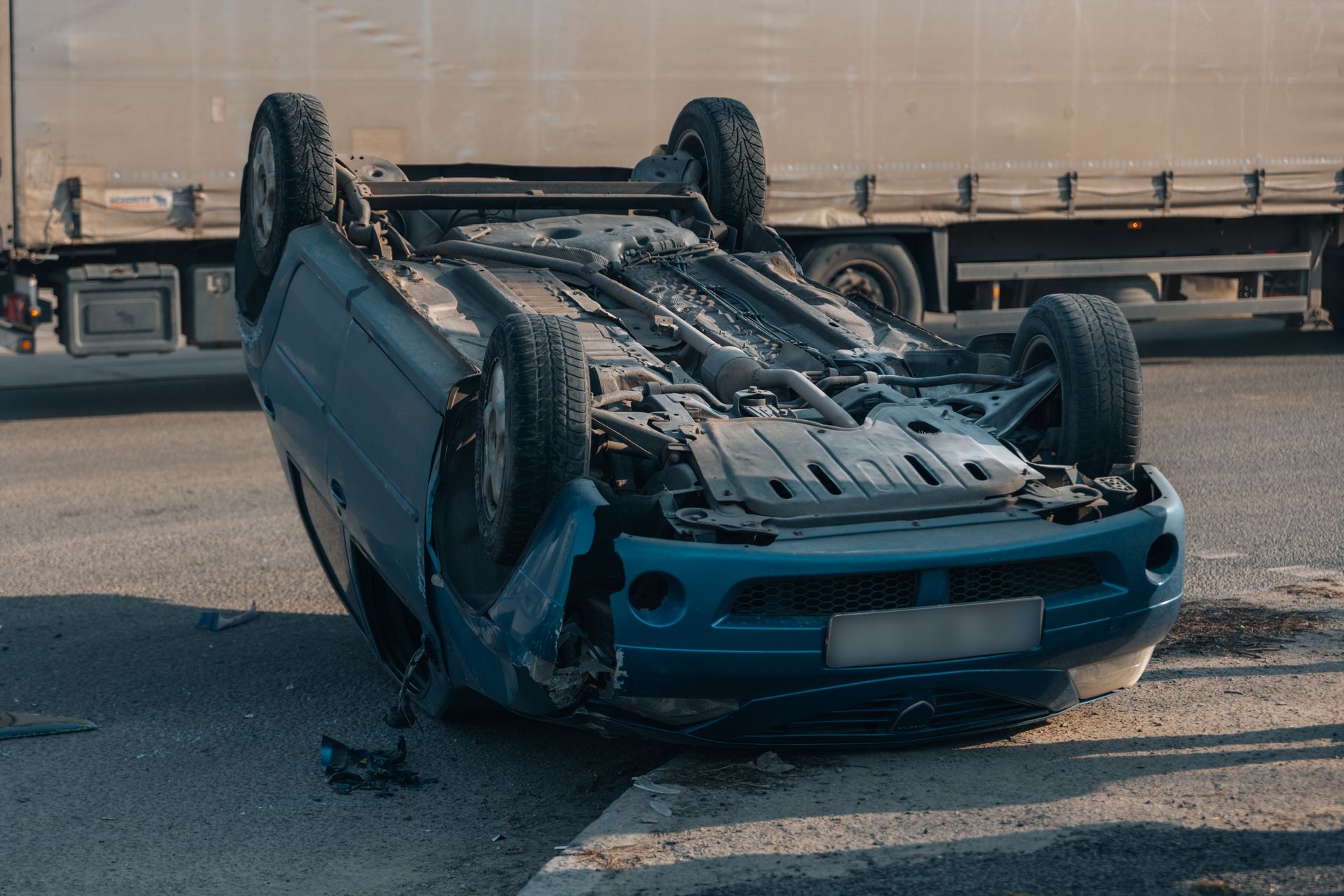Blue car overturned on a road, next to a large truck.