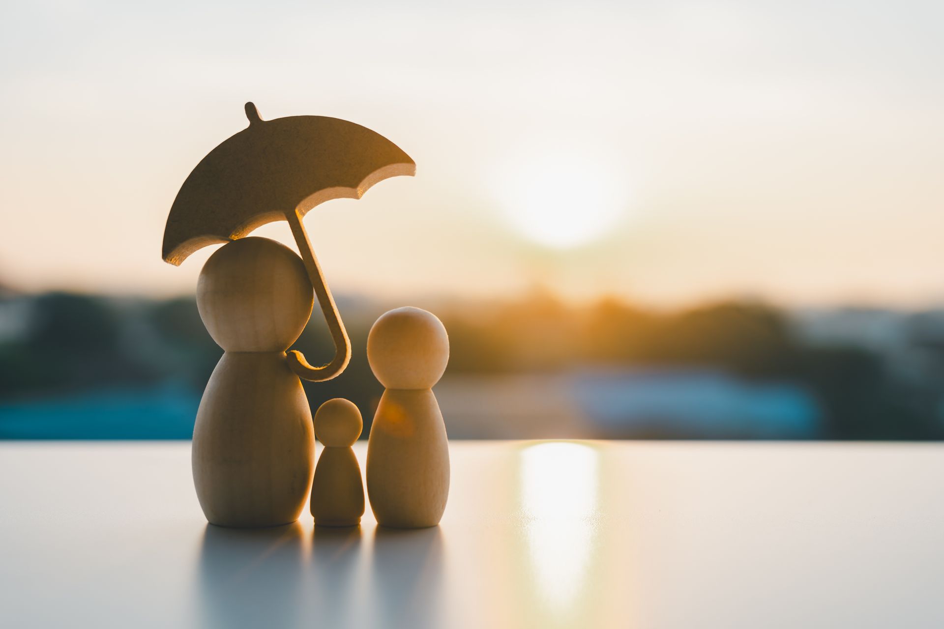 Wooden family figures under an umbrella, silhouetted by the sunset.
