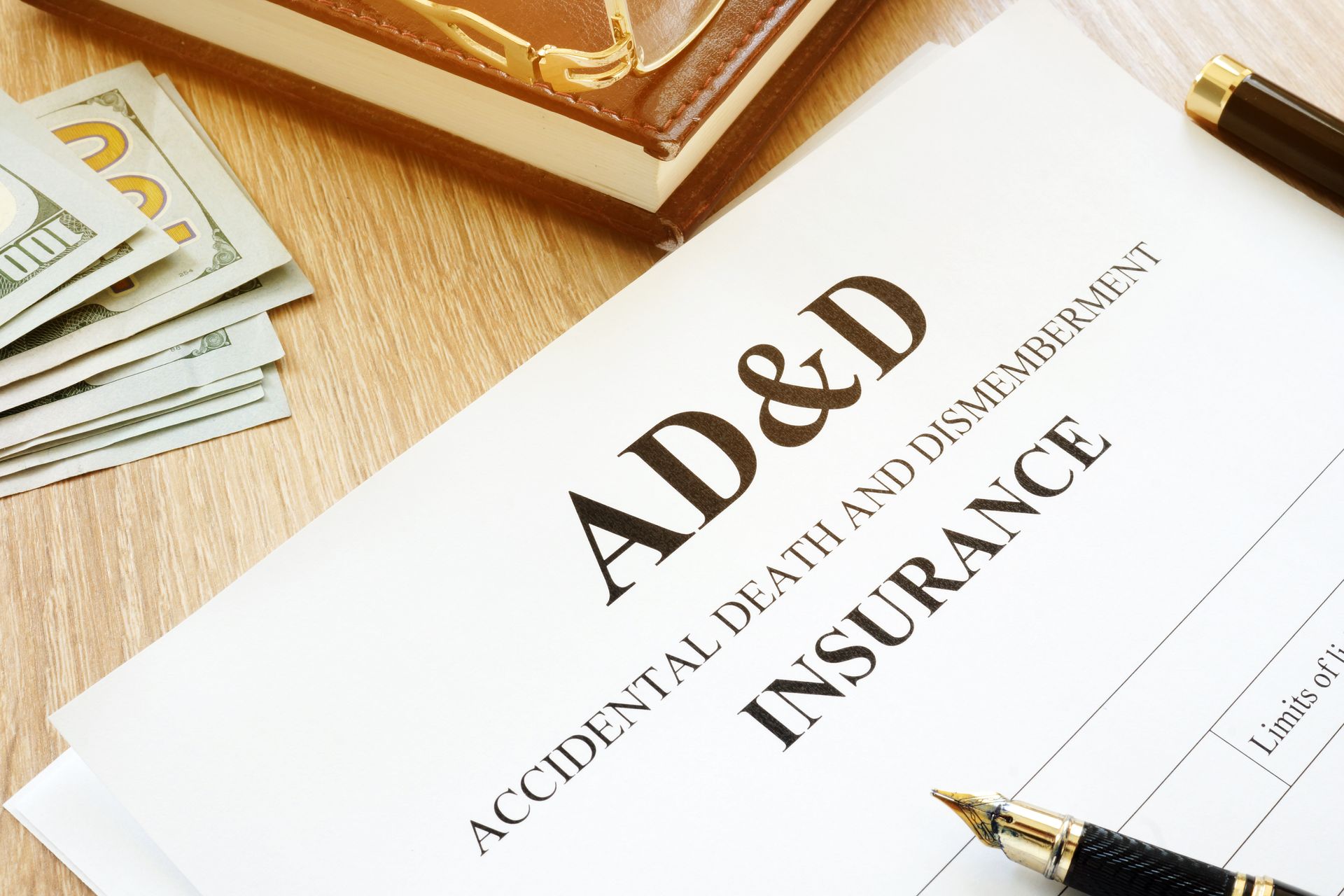 AD&D insurance document with pen, money, glasses, and a book on a wooden surface.