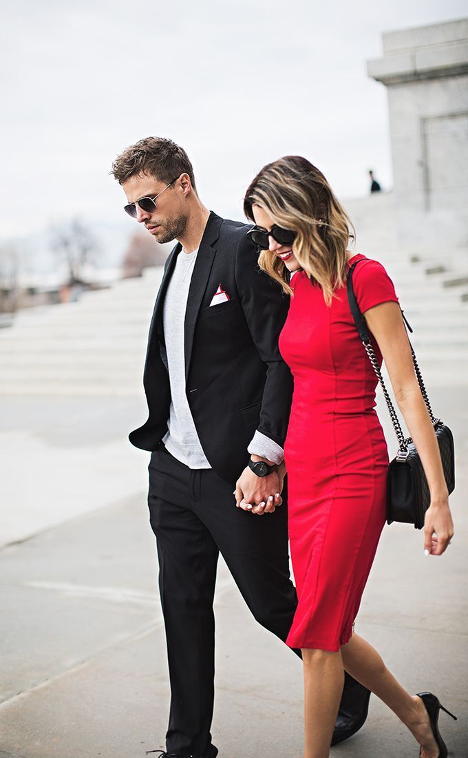 Couple walking hand in hand outdoors, dressed in black and red, on a bright paved walkway