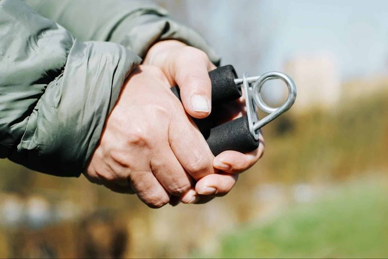 Hands squeezing a black hand gripper outdoors.