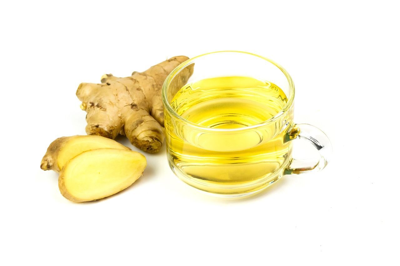 Glass cup of yellow ginger tea beside fresh ginger root slices on a white background
