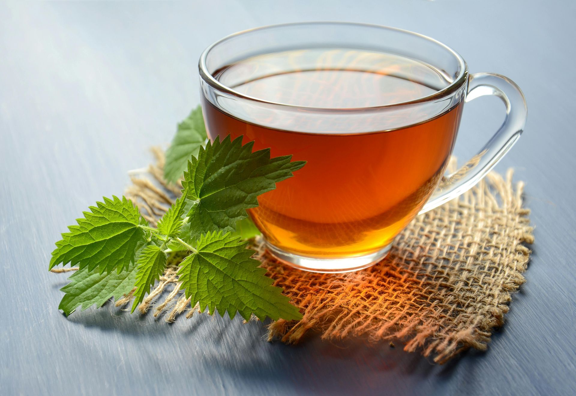 Glass mug of tea with a sprig of green leaves on a burlap coaster.