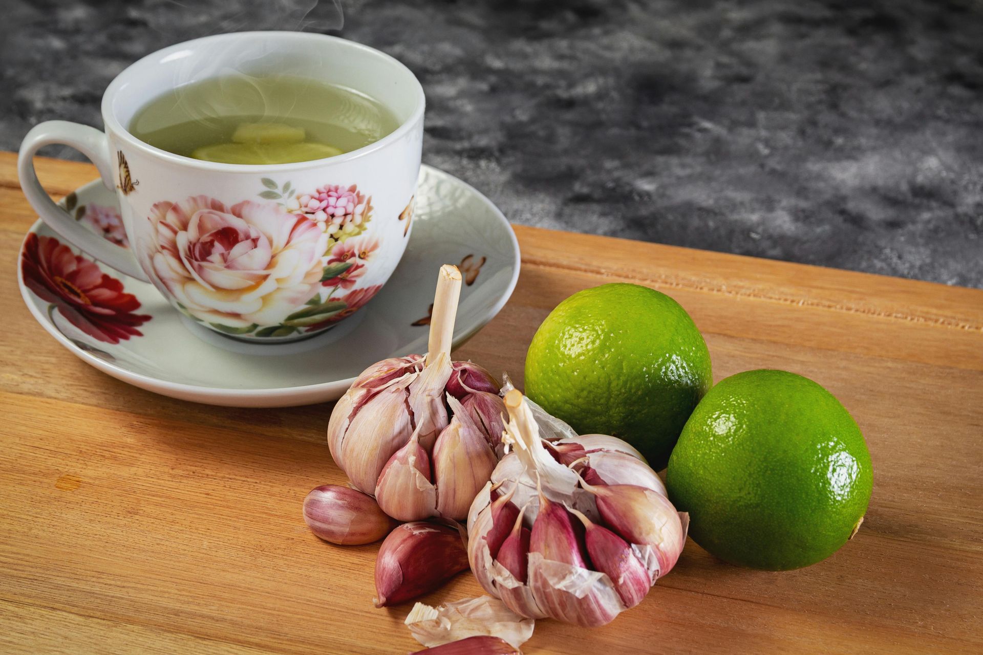 Herbal tea cup with garlic bulbs and two limes on a wooden board