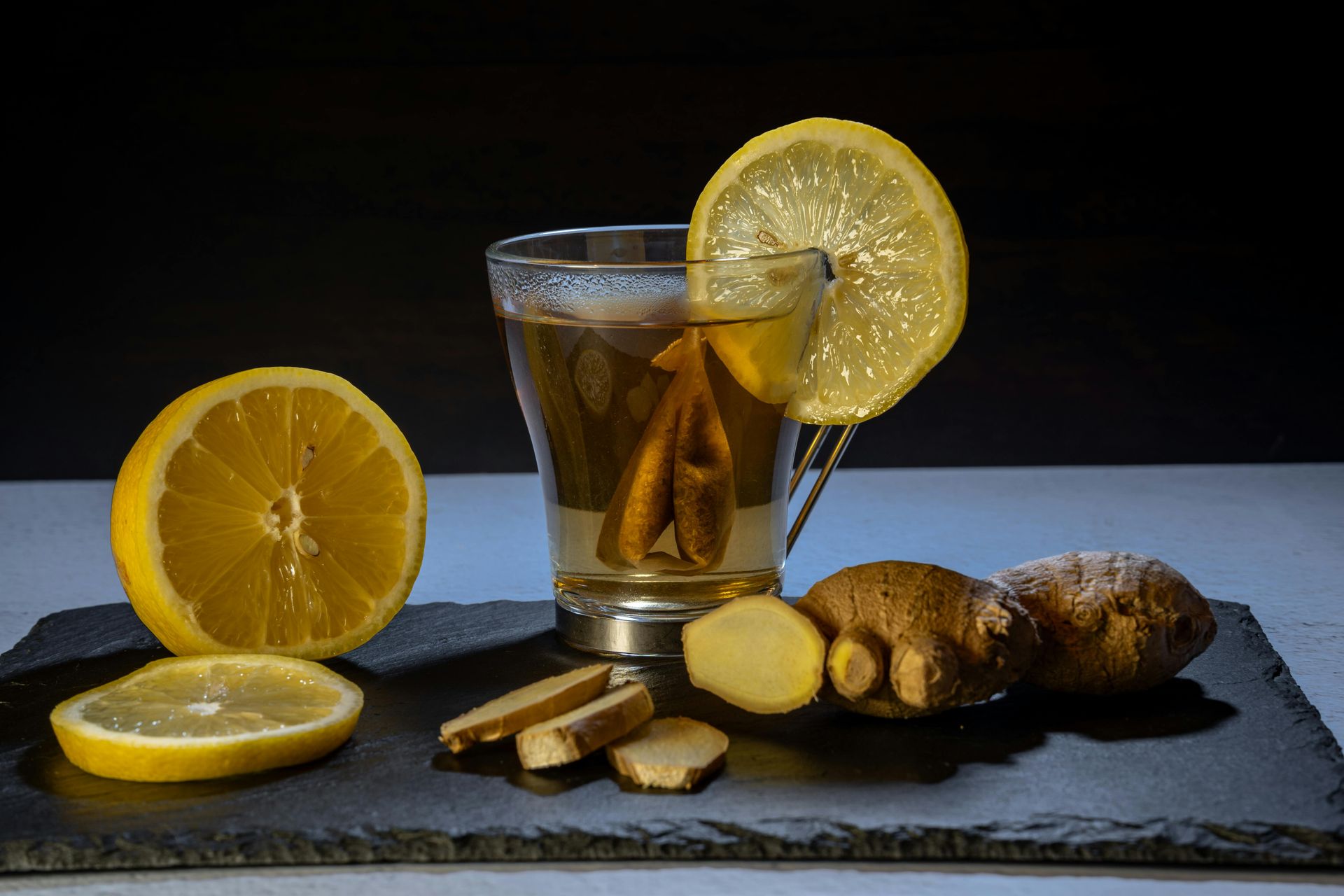 Glass of tea with lemon and ginger on a slate board.