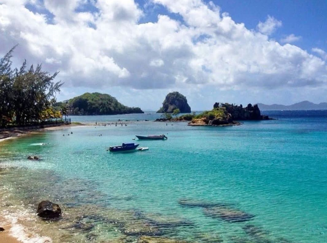 Turquoise tropical bay with small boats, rocky islands, and a cloudy sky