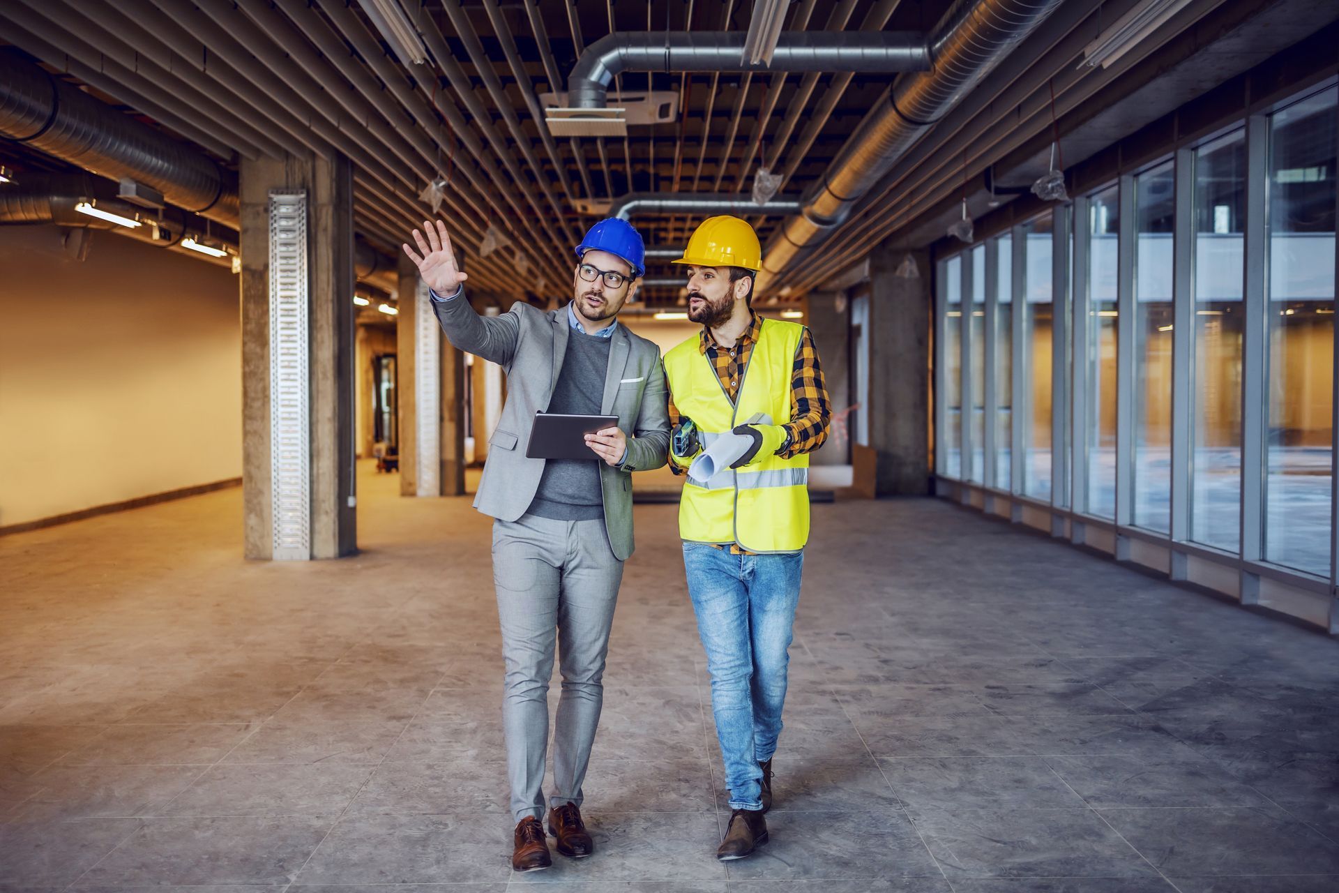 Un homme et un ouvrier du bâtiment marchent dans un bâtiment en construction.