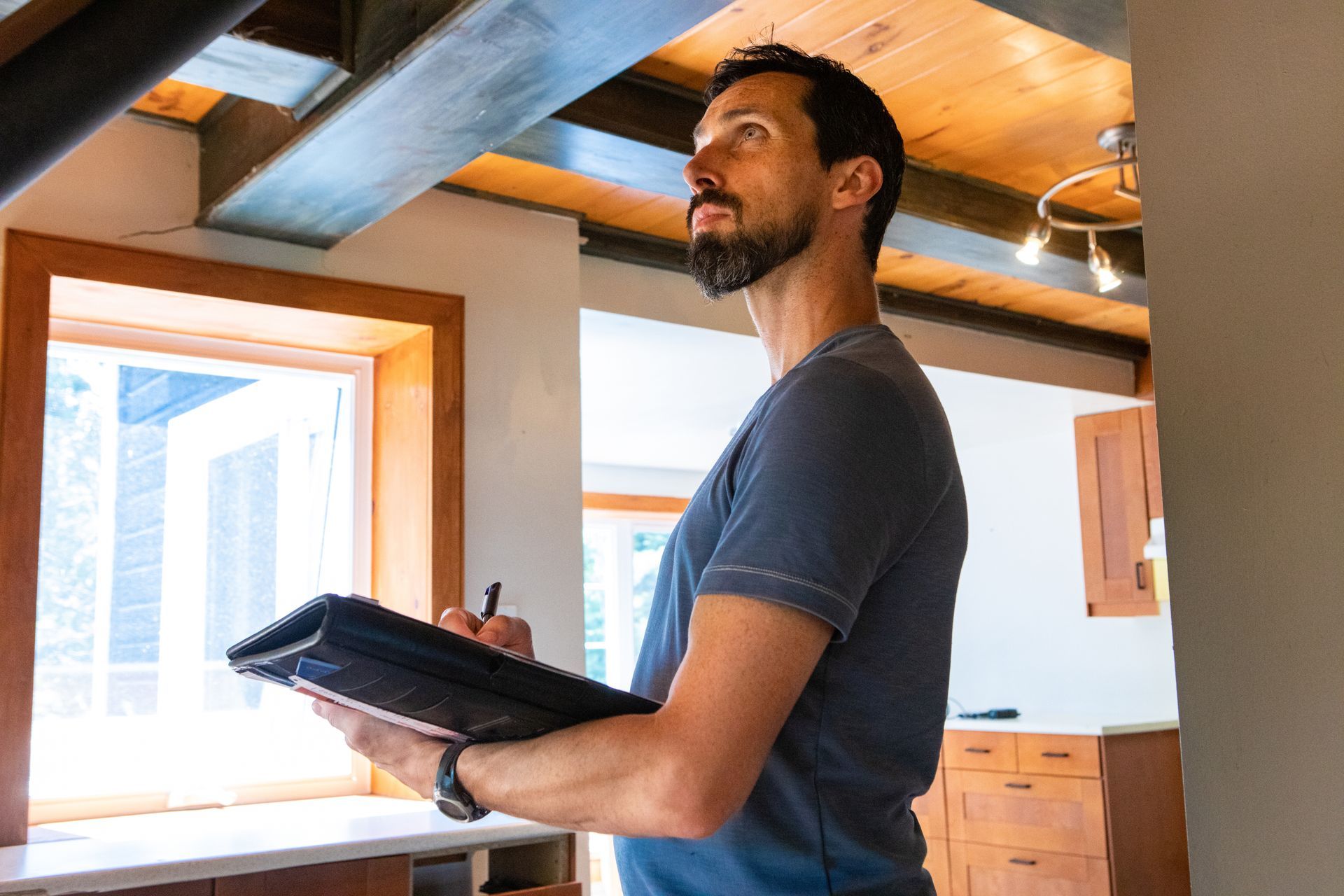 Un homme inspecte une pièce, un bloc-notes à la main. Barbu, il lève les yeux au ciel, évaluant l'espace.
