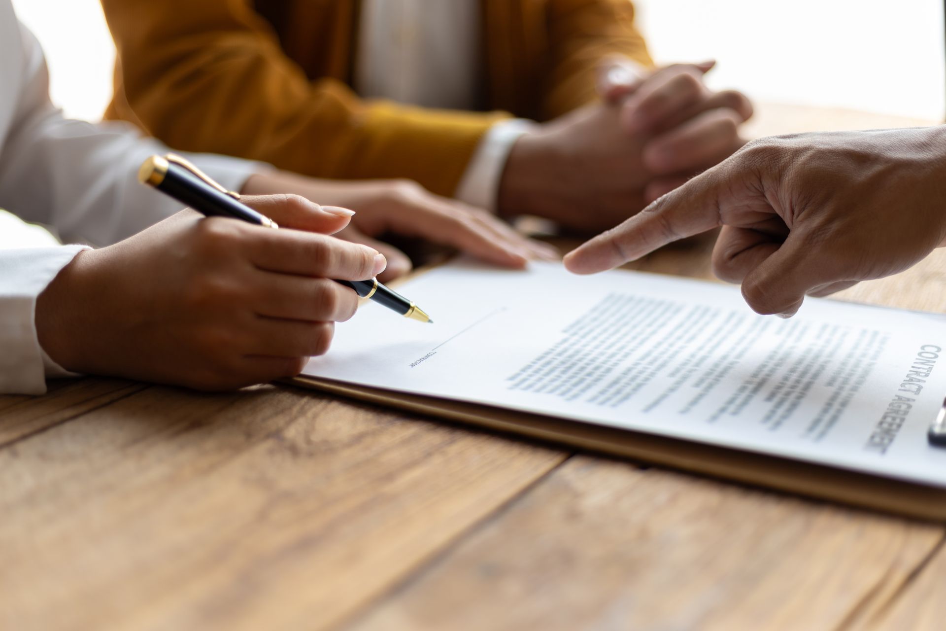 Une personne signe un document, une autre personne le désigne du doigt, sur une table en bois.