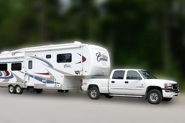 Large dual axel pull behind camper attached to a white GMC truck. 