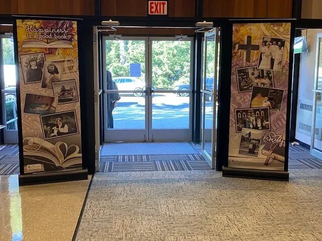 Lobby entrance with glass doors, an exit sign, and two poster displays on either side.