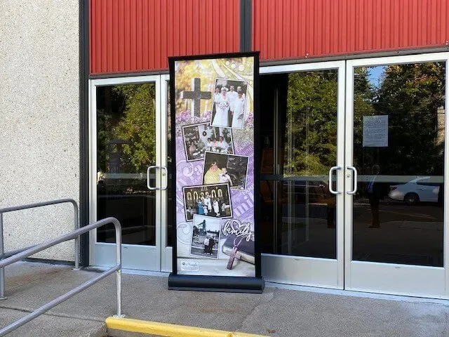 Glass storefront entrance with red siding and a memorial collage banner beside the doors