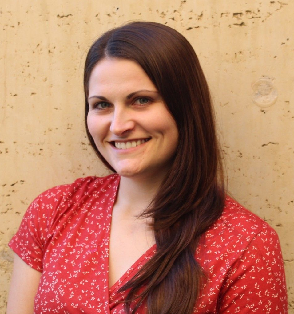 Smiling woman in a red patterned blouse standing against a beige textured wall
