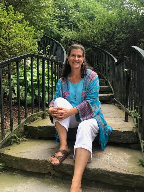 Woman sitting on stone steps in a lush garden, smiling and holding a white ball