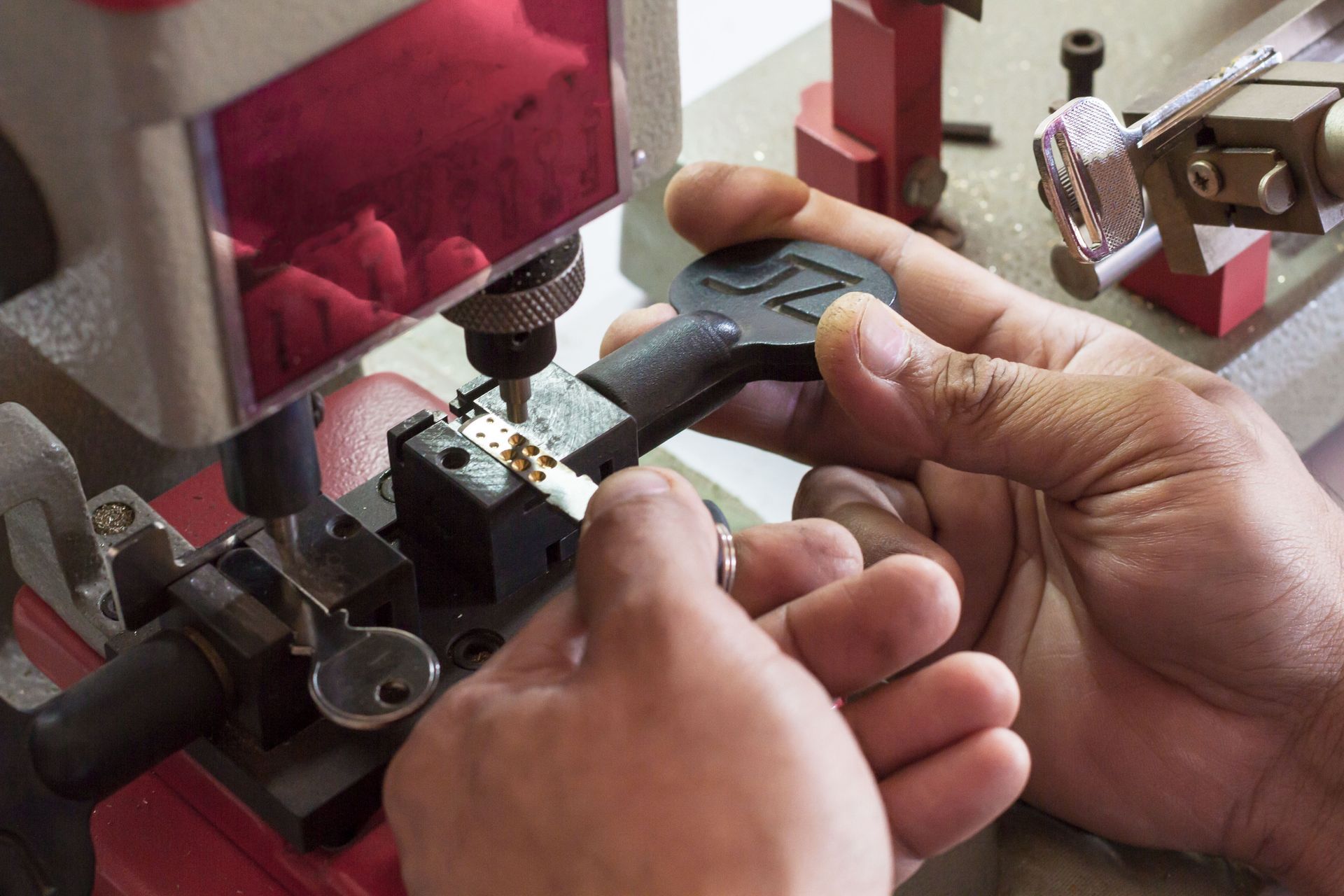 Hands adjusting a black tool under a red machine in a workshop