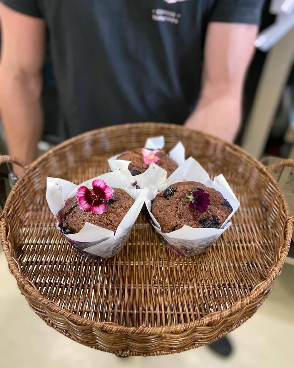 A Man is Holding a Basket of Muffins With Flowers on Them — Swish Cafe in Ballina, NSW