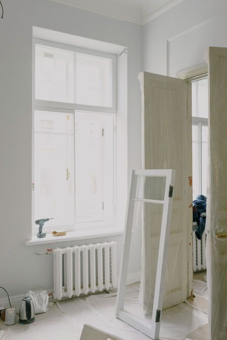 Stanza luminosa con ampia finestra, termosifone e specchio o cornice appoggiati, in un interno minimalista.