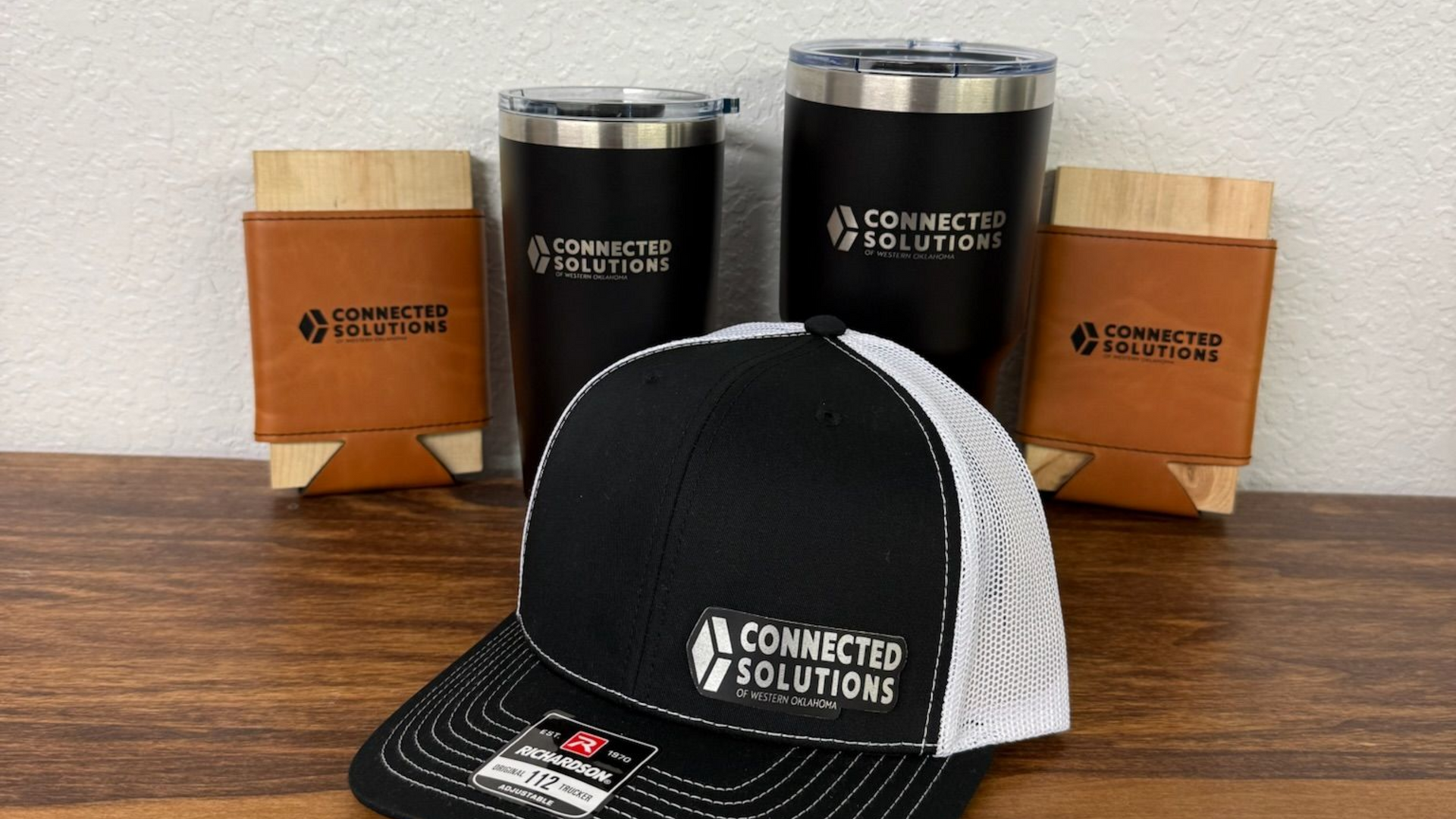 Promotional items with the "Connected Solutions" logo: a hat, two tumblers, and two koozies.