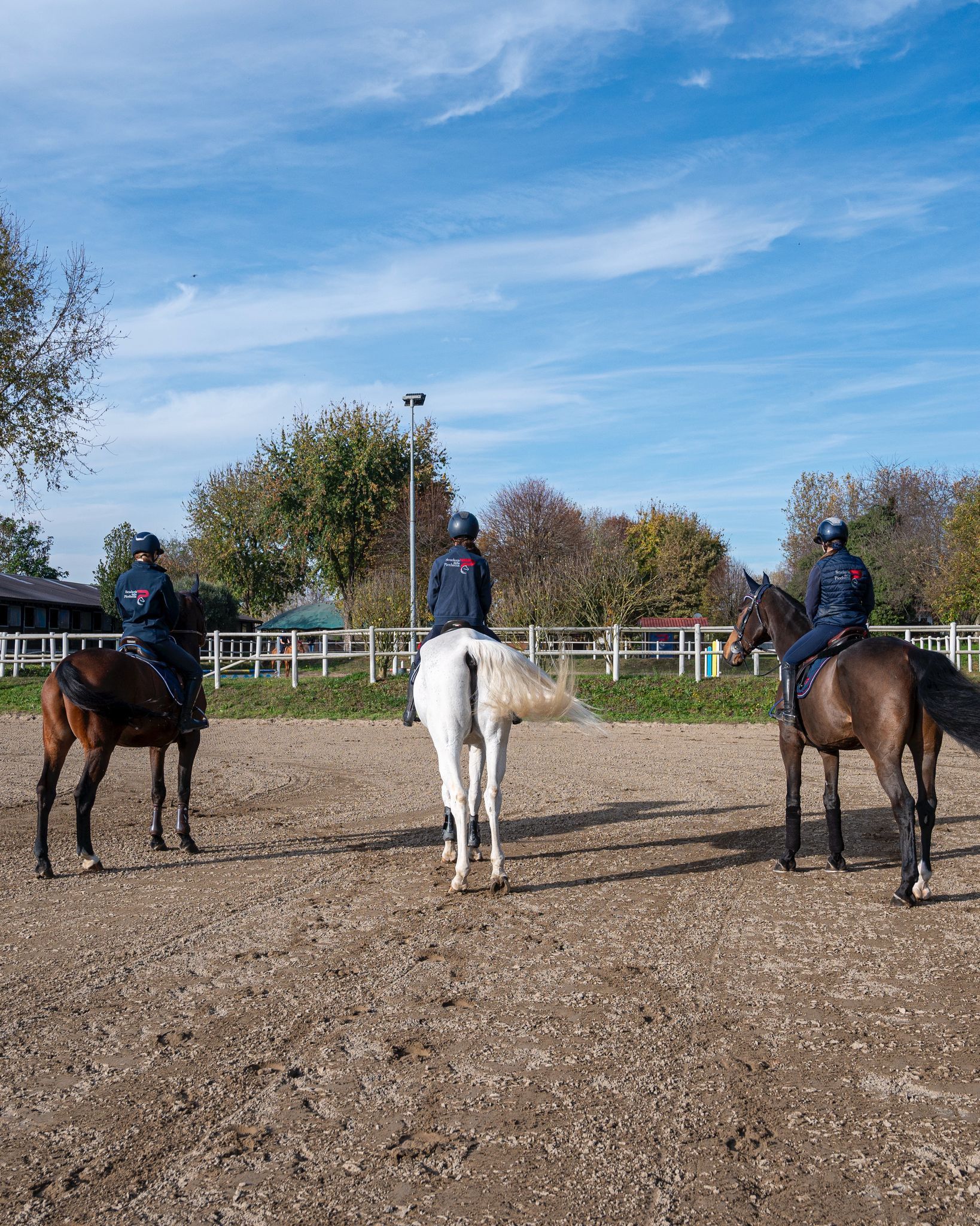 Due persone a cavallo in una zona erbosa, con indosso caschi da equitazione e sottosella colorati.