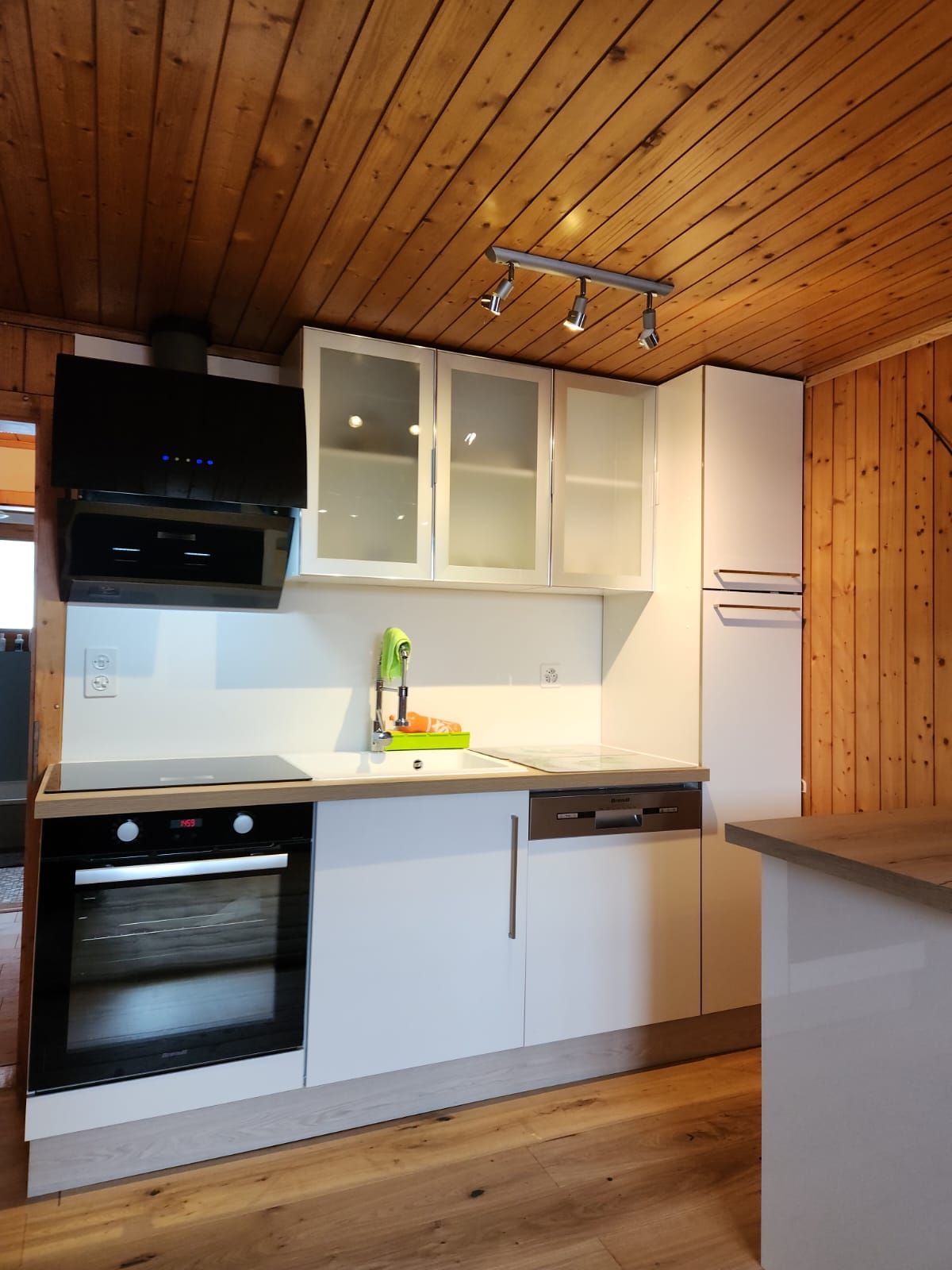 Cuisine moderne avec armoires blanches, four noir, plafond en bois et comptoir clair