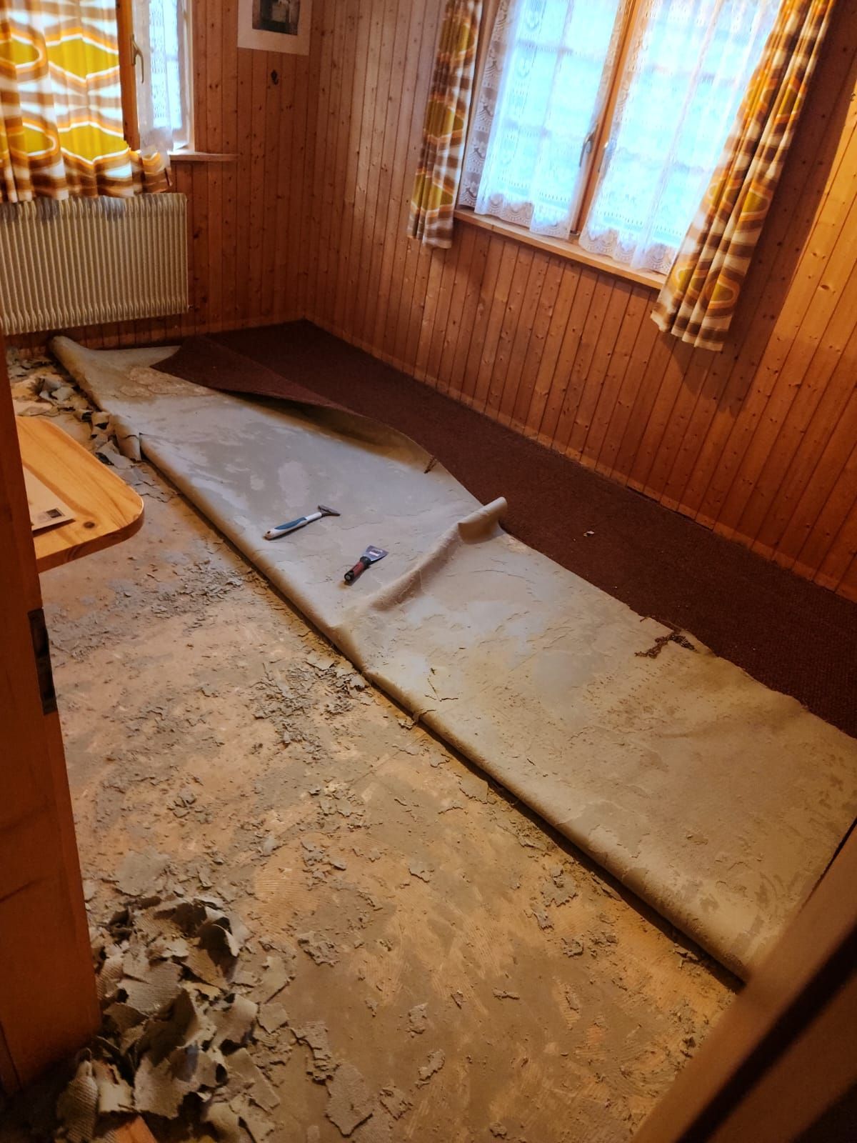 Travaux de rénovation en cours dans une pièce lambrissée, avec des planches de parquet retirées et des outils éparpillés sur le revêtement de sol.