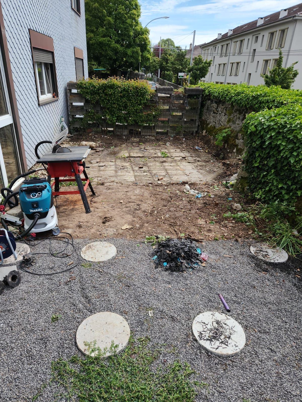 Terrasse arrière avec gravier, dalles de pierre, arbustes et une petite table à côté d'une maison