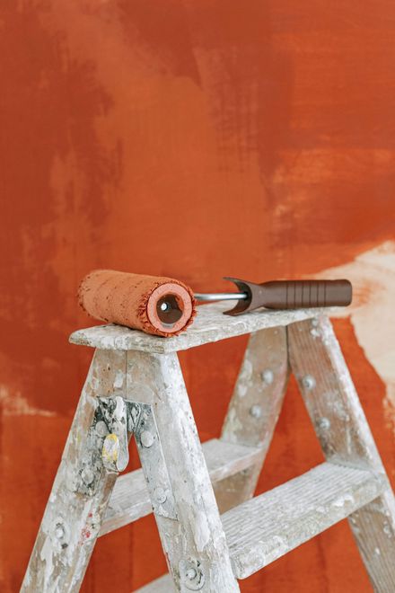 Rouleau et pinceau sur un escabeau blanc devant un mur orange