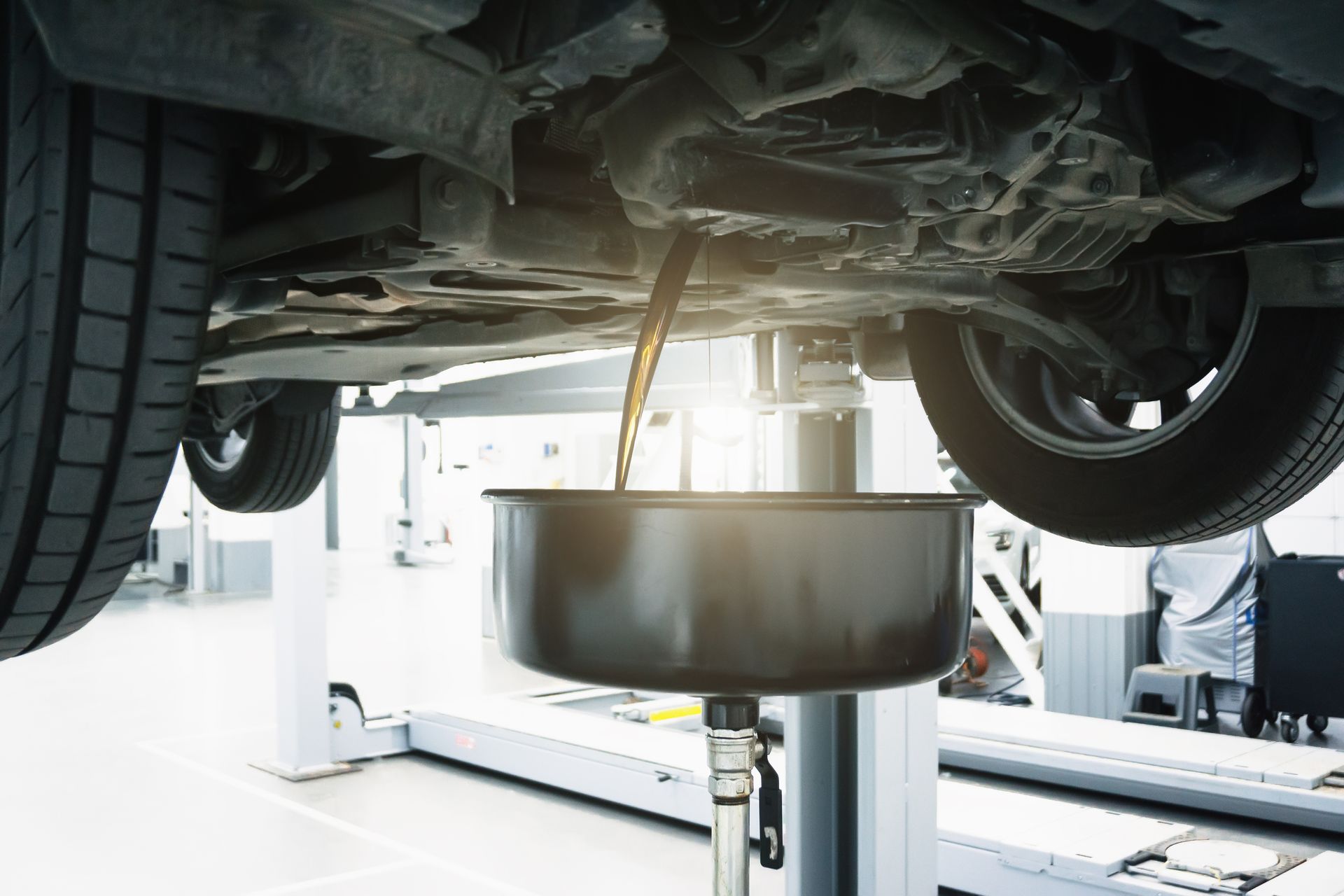 Car on a lift, oil draining into a pan underneath, in a mechanic's garage.
