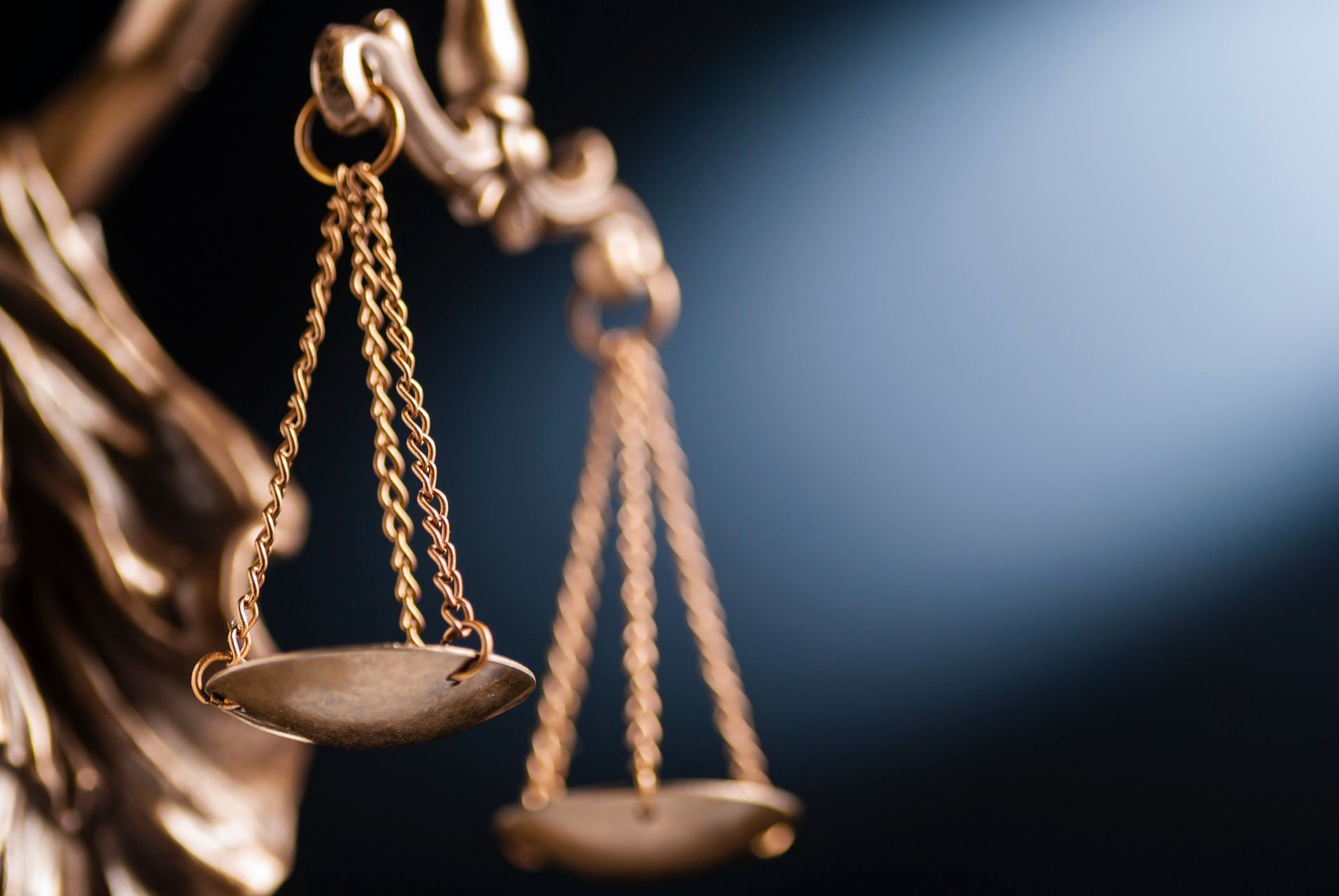 Close-up of bronze scales of justice against a blurred blue background