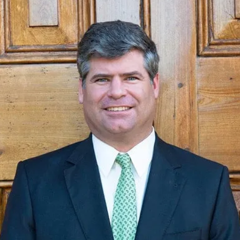 Smiling man in a dark suit and green tie standing in front of wooden doors