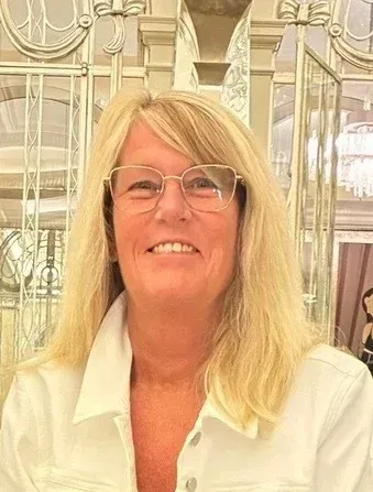 Smiling woman in a white shirt and glasses standing in an elegant indoor setting