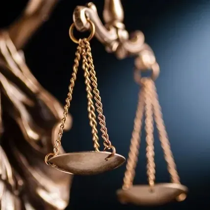 Close-up of bronze balance scales in a dark courtroom setting