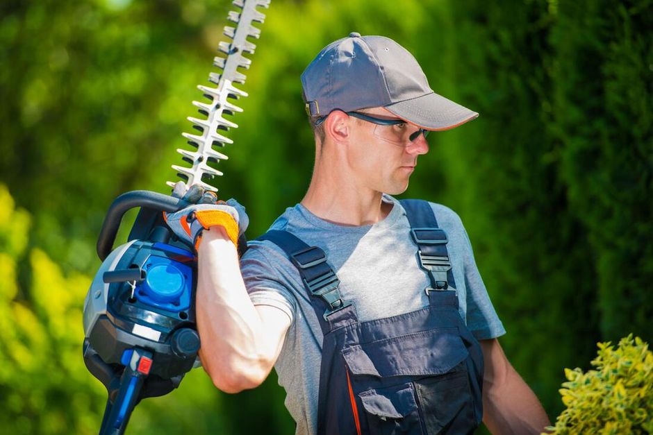 Man with safety glasses holding chainsaw behind him