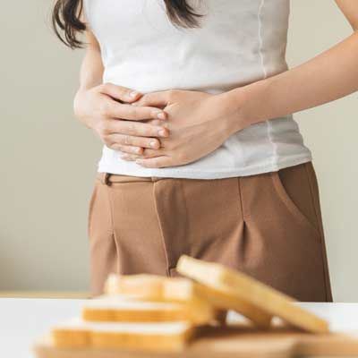 Person with Celiac Disease holding their stomach above sliced bread on a table, suggesting digestive discomfort.