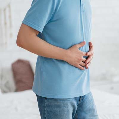 Person in a blue shirt clutching their stomach indoors, suggesting Inflammatory Bowel Disease