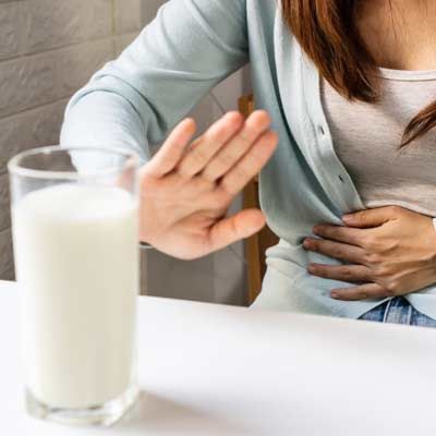 Person holding stomach and raising hand to stop a glass of milk on a table because of Lactose Intolerance