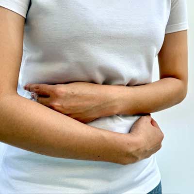 A person holding their stomach with Post-Infection Digestive Issues. shes wearing a white shirt on a plain background
