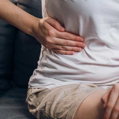 a woman's hand clutching her side from fatty liver disease while they sit on a couch, suggesting abdominal pain