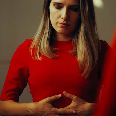 Woman in a red shirt with Upper Abdominal Pressure holding her hands over her stomach, looking down thoughtfully.