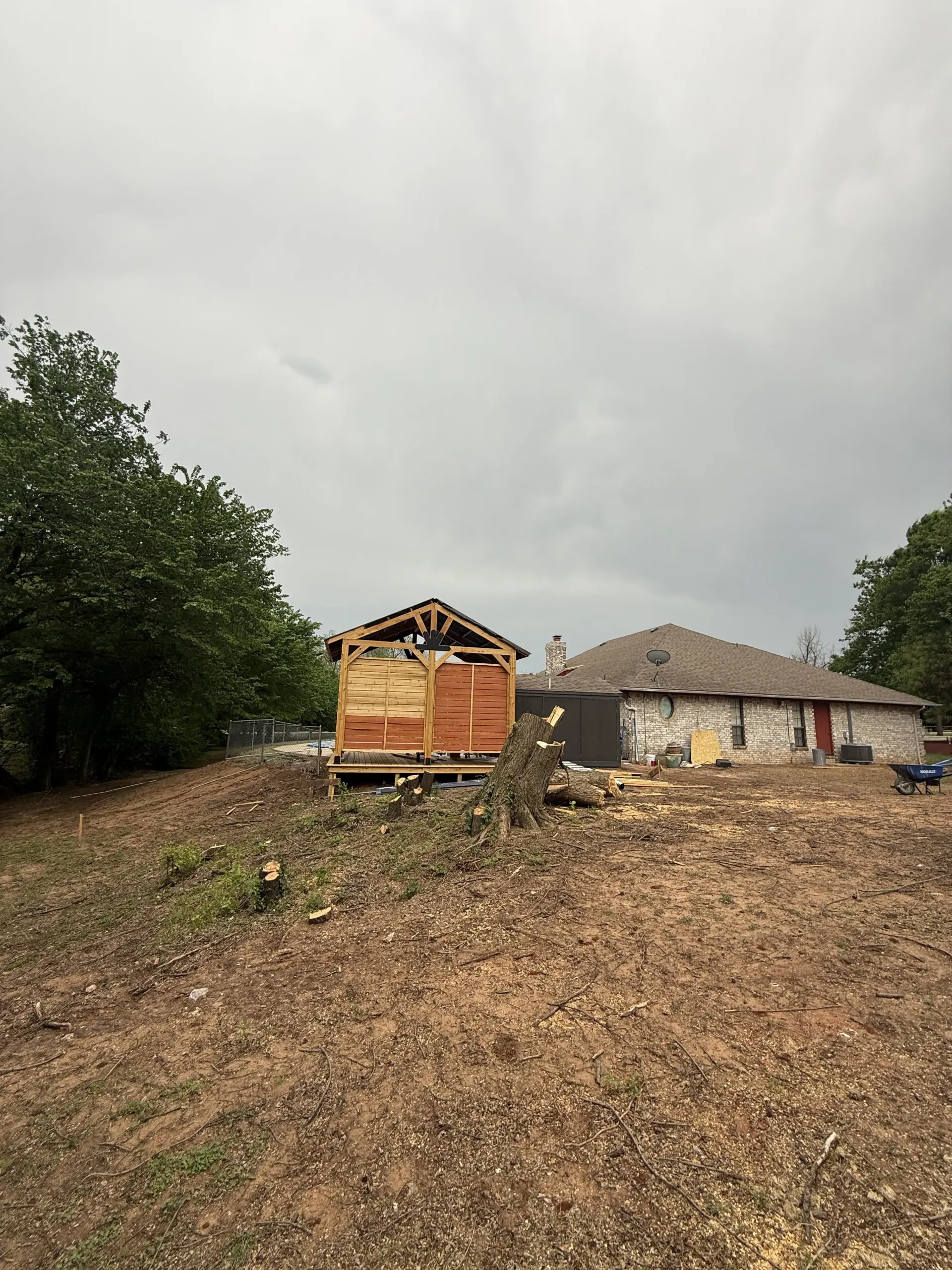 Rustic rural homestead with a wooden structure, stone house, and muddy yard under an overcast sky