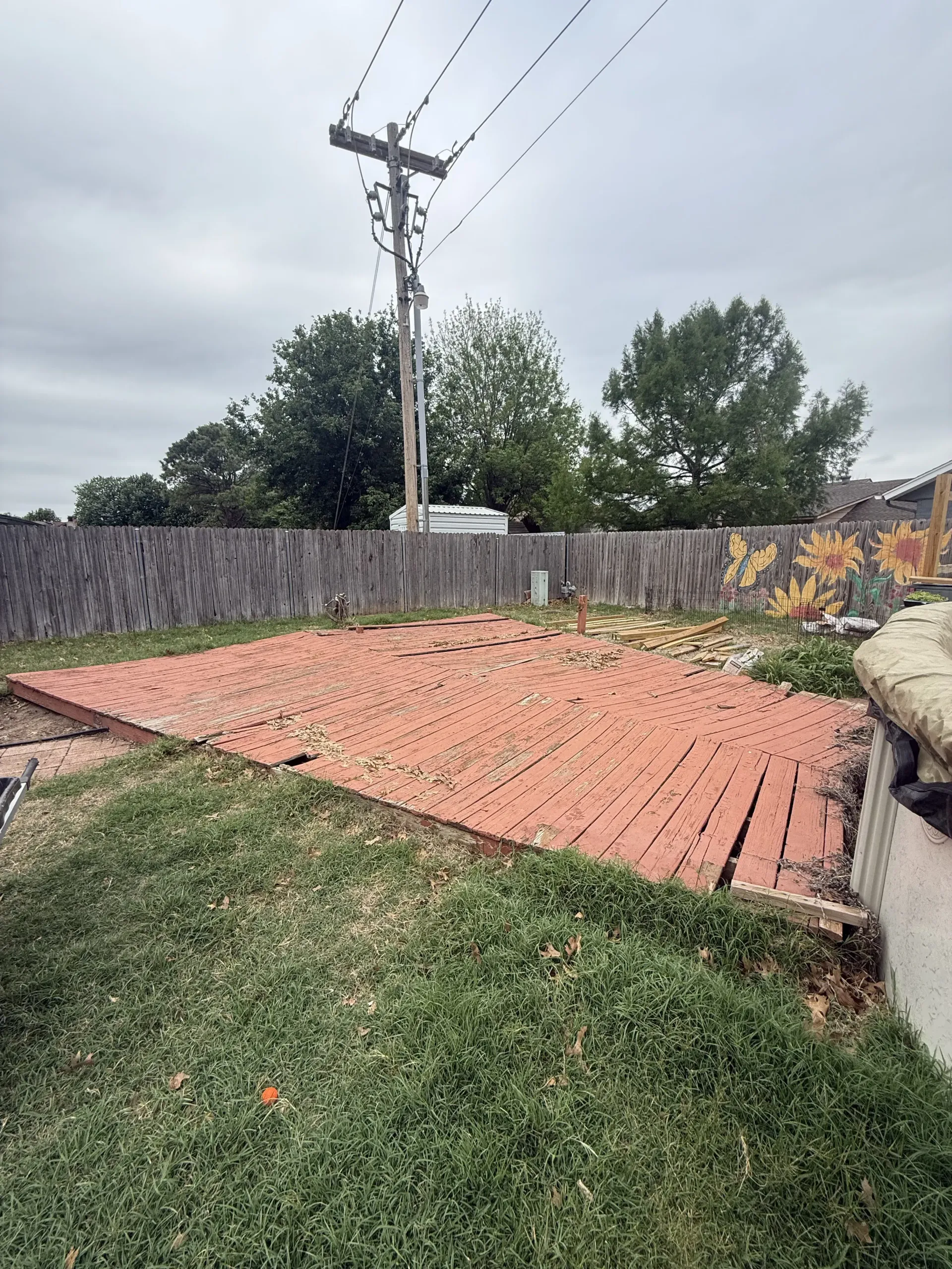 Backyard with a brick patio, grass, wooden fence, and power pole under a cloudy sky