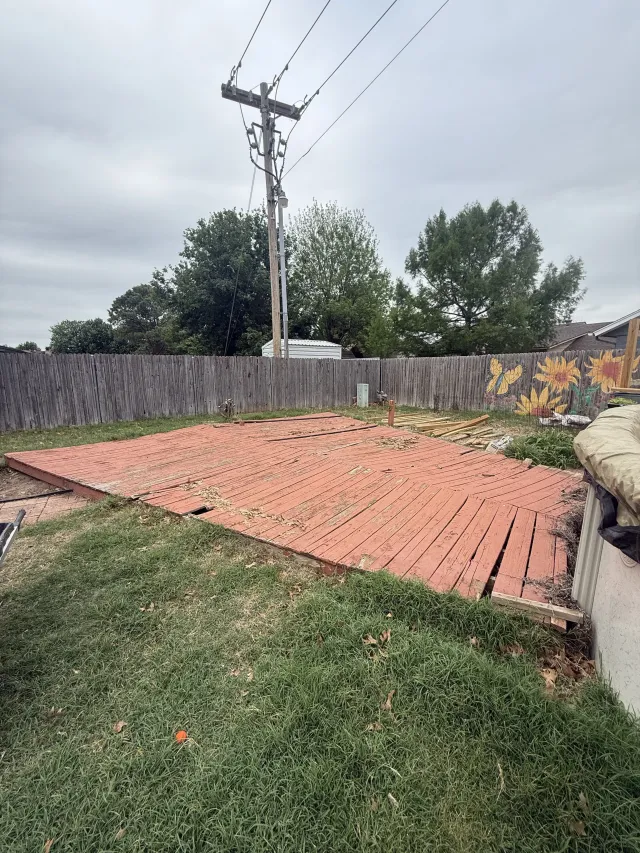 Backyard with a brick patio, grass, wooden fence, and power pole under a cloudy sky