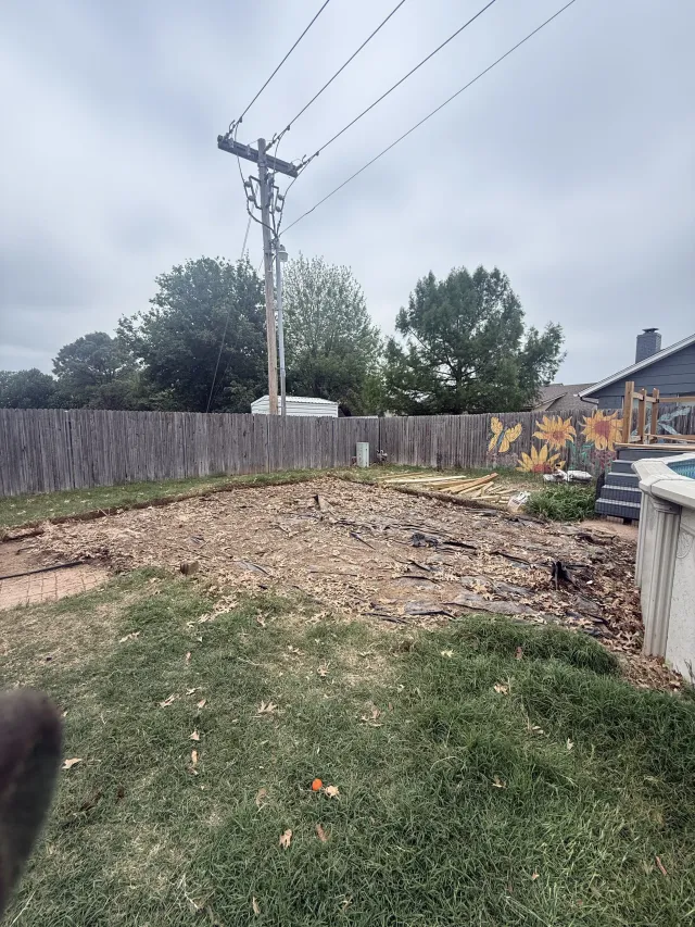 Backyard with a utility pole, wooden fence, grass, and a cleared dirt area under cloudy skies
