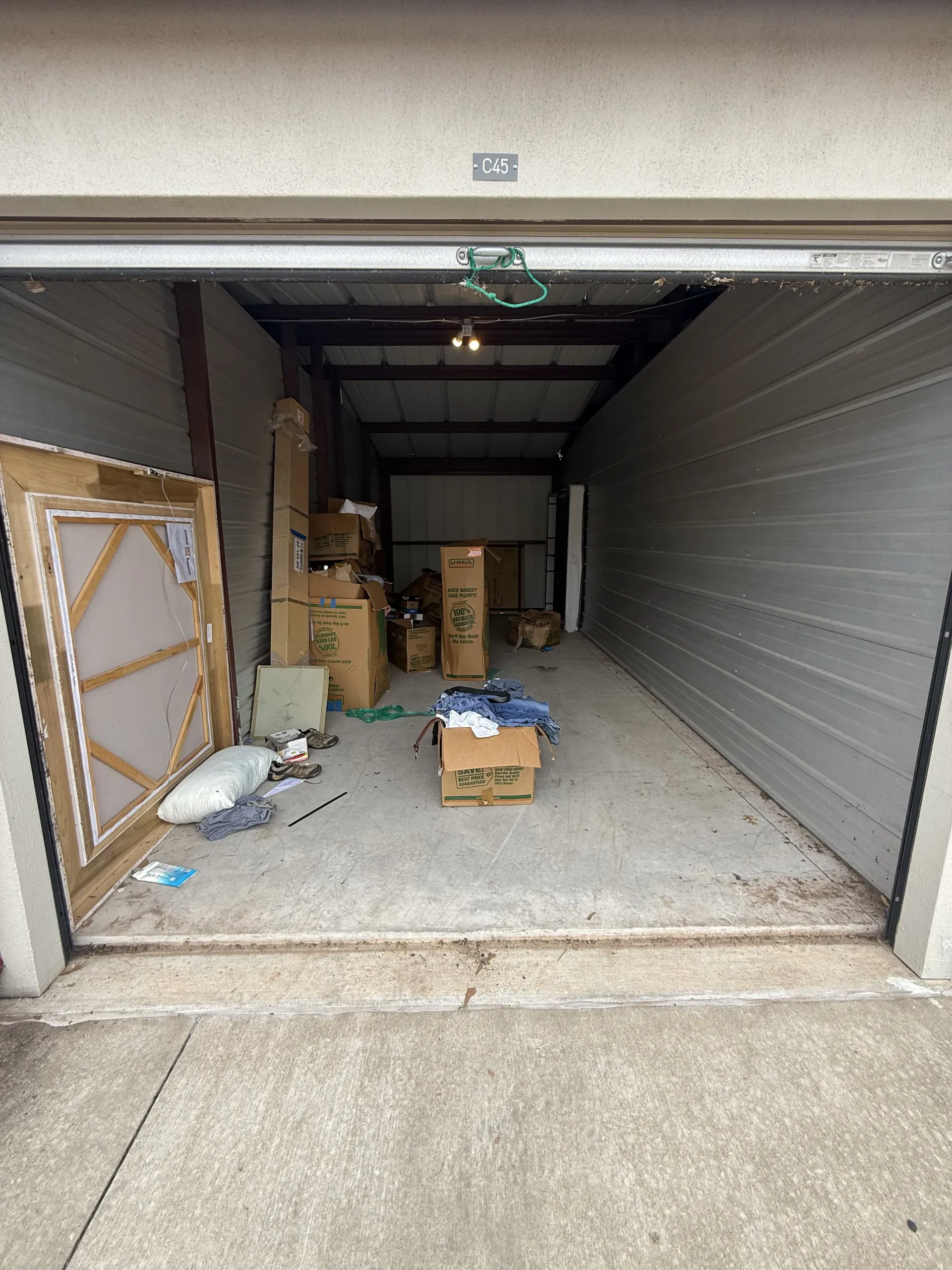 Open garage unit with cluttered storage boxes, frames, and debris on the floor.