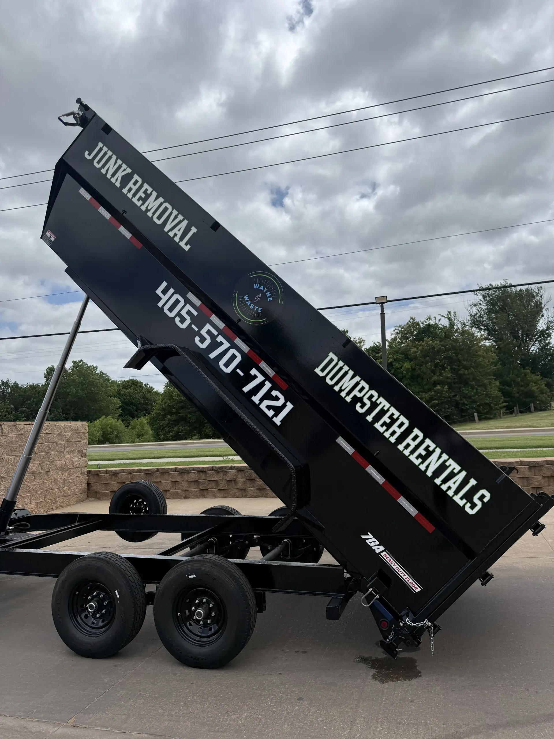 Black dump trailer with raised bed and white rental lettering on a cloudy roadside.